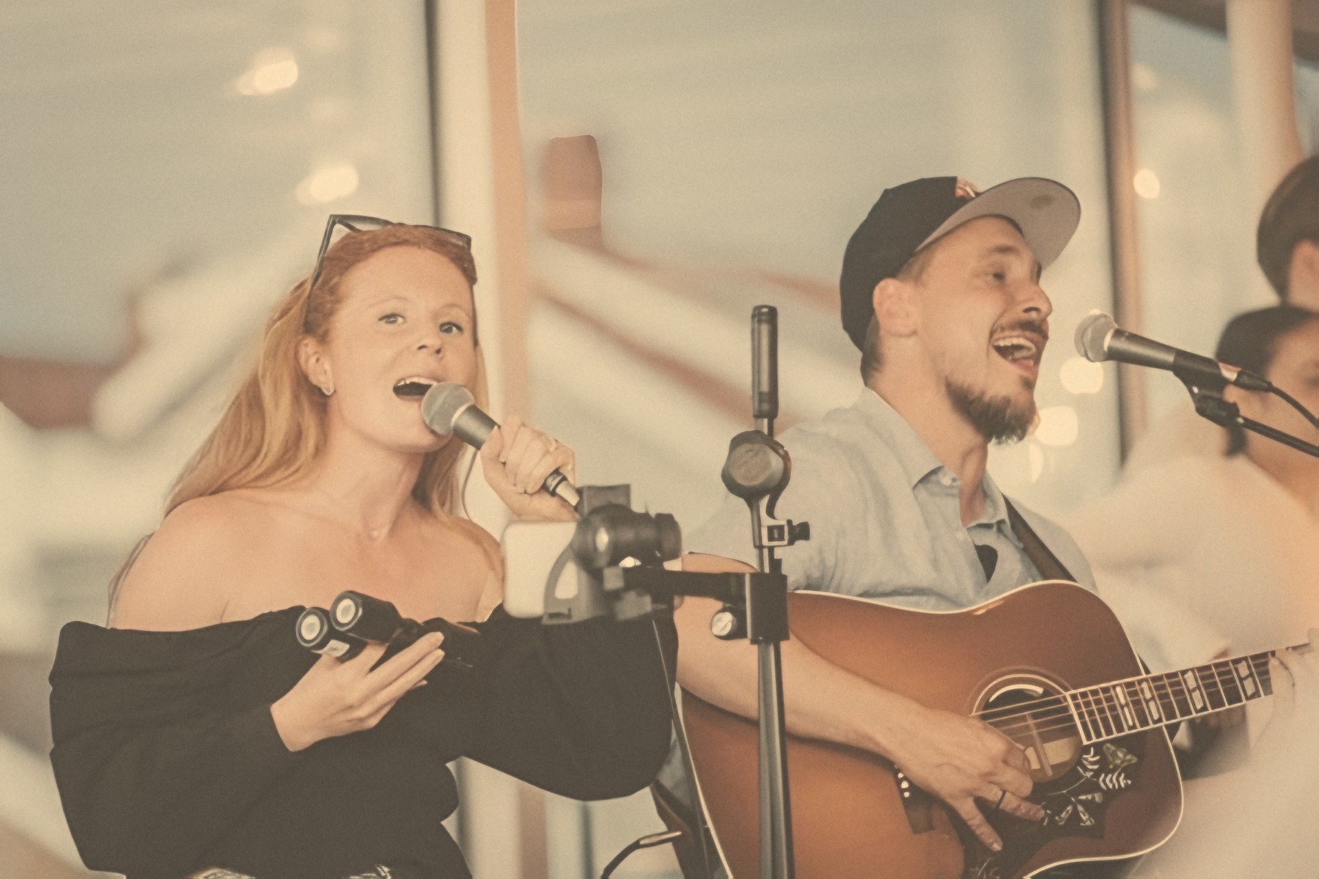 Two singers with an acoustic guitar performing live at a venue
